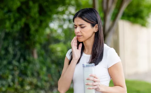 A woman feeling her jaw after experiencing pain from a broken tooth.